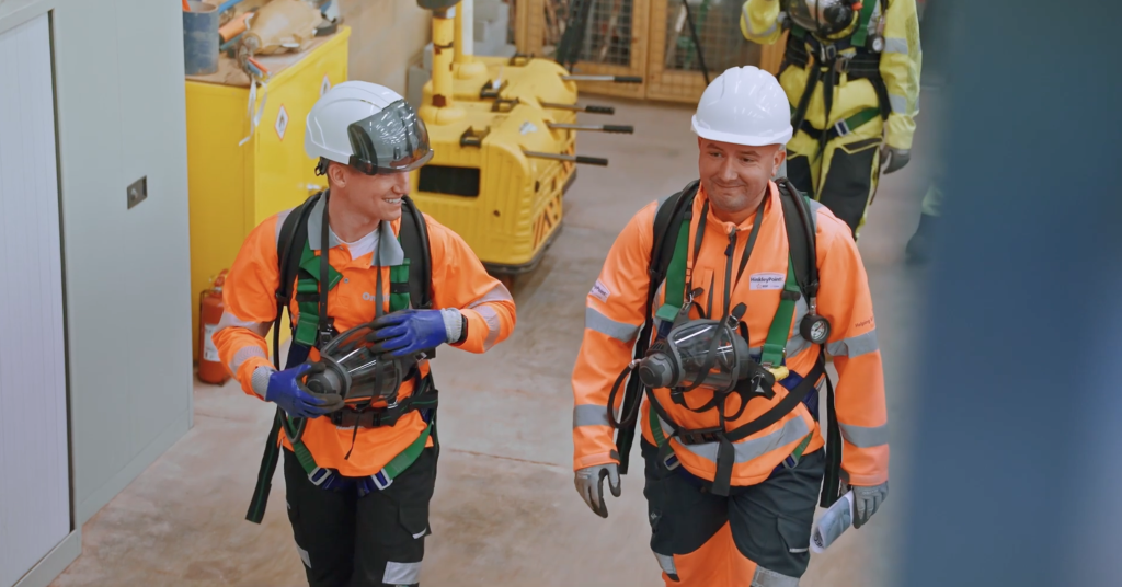 Two workers in safety harnesses and hard hats in an industrial building
